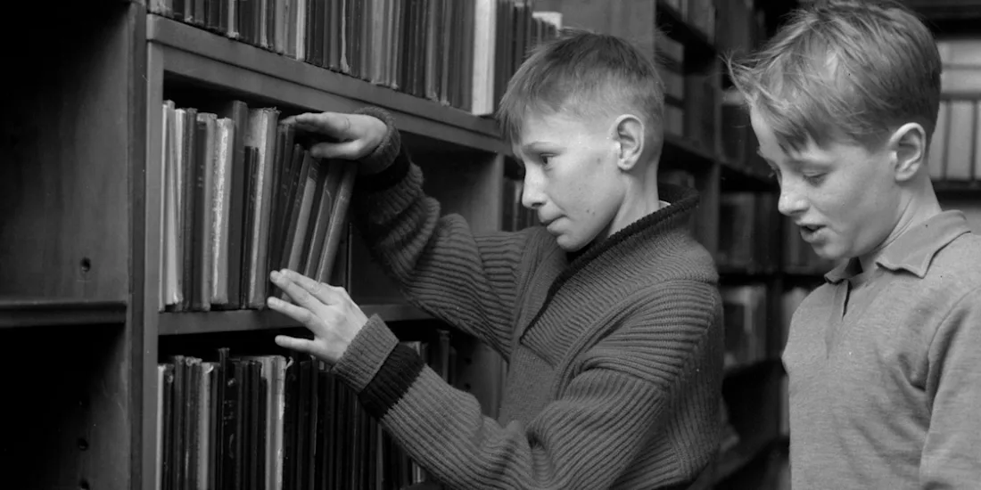 Two young boys look at books on a bookshelf