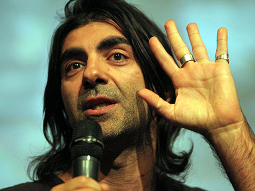 barevná fotografie Fatiha Akina, který drží mikrofon a zvedá jednu ruku