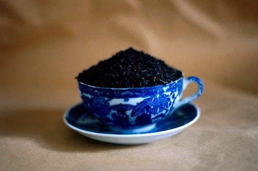 a tea cup on a saucer in white enamel with blue glazing is filled with heaping black tea leaves.
