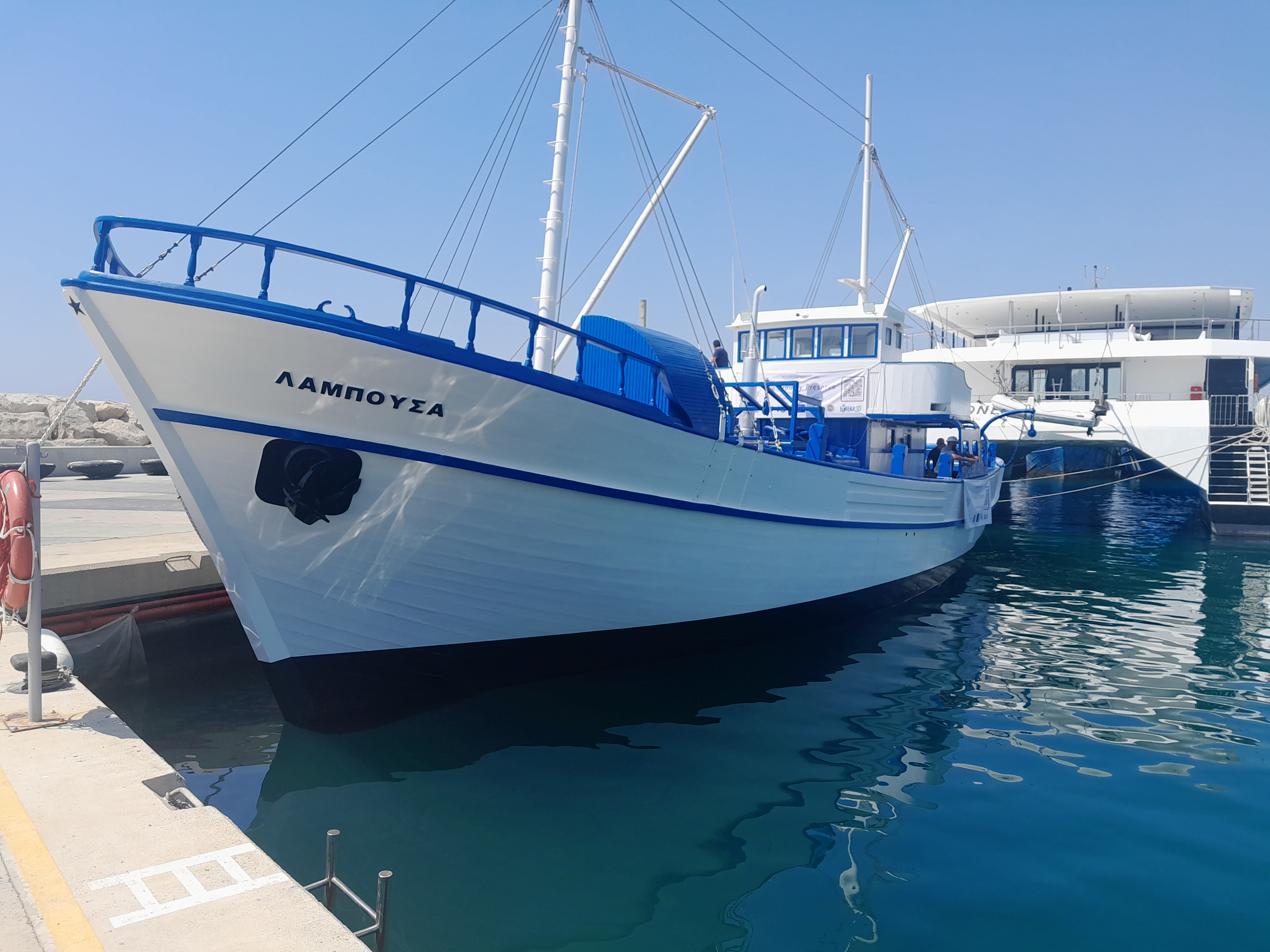 A white and blue fishing trawler sits in the water at a dock in Cyprus