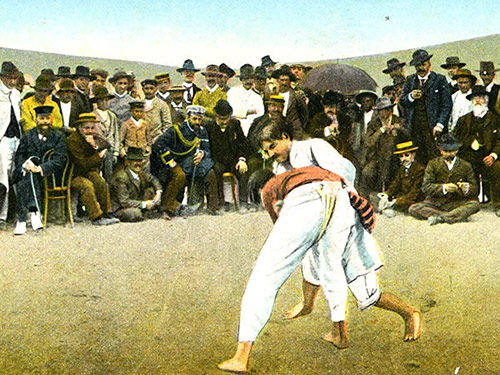 barevný obrázek dvou mužů zápasících v bílých kostýmech sledovaných davem