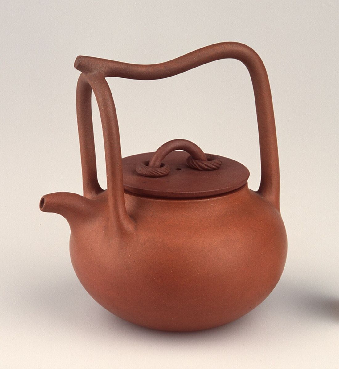 a clay teapot with a small spout and large upright handle
