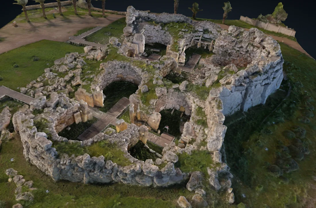 Aerial view of ancient stone ruins with circular walls and grassy areas, surrounded by trees and pathways.