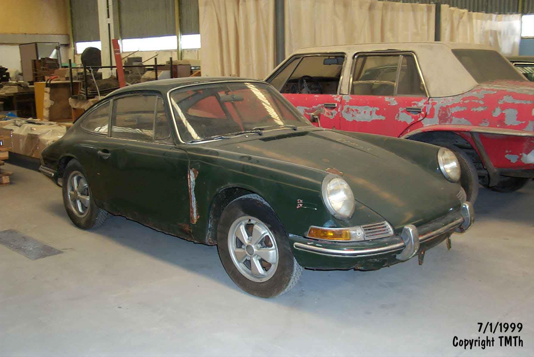 a green Porsche car in a room, parked in front of a damaged red car.