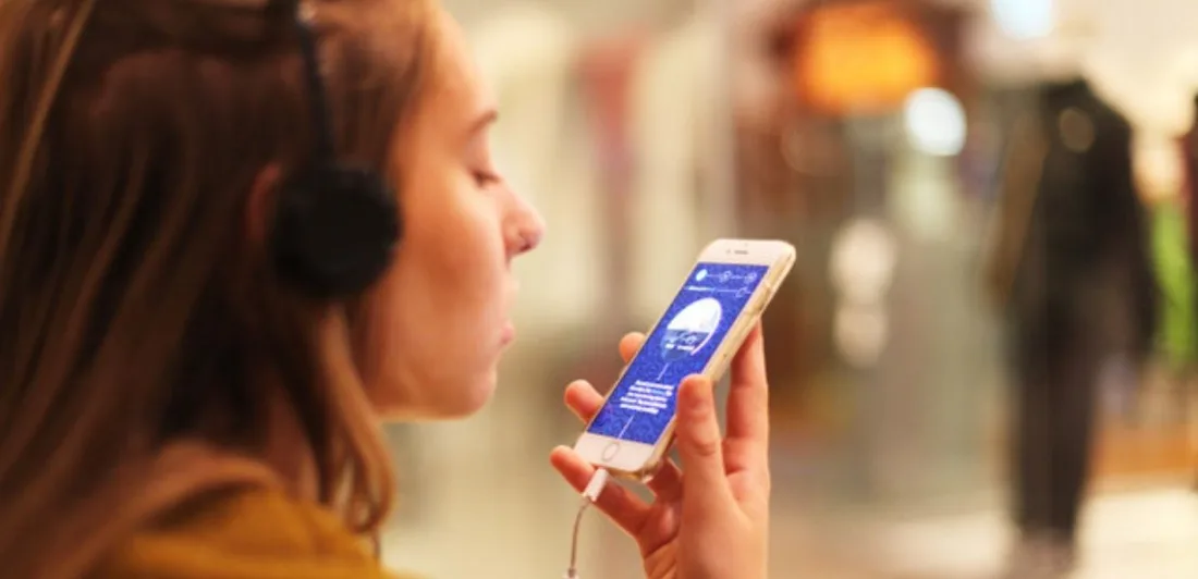 A woman wearing headphones speaking into a phone held in her hand
