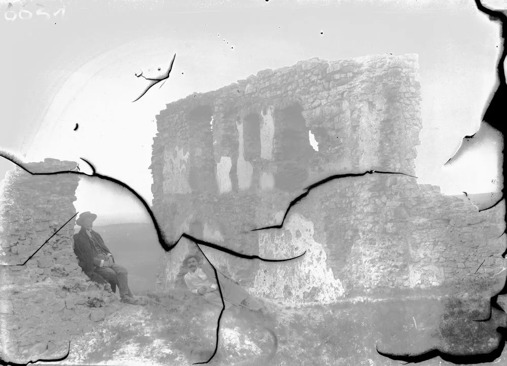 Black and white photograph of castle ruins with a man sitting in front, on a broken glass negative 