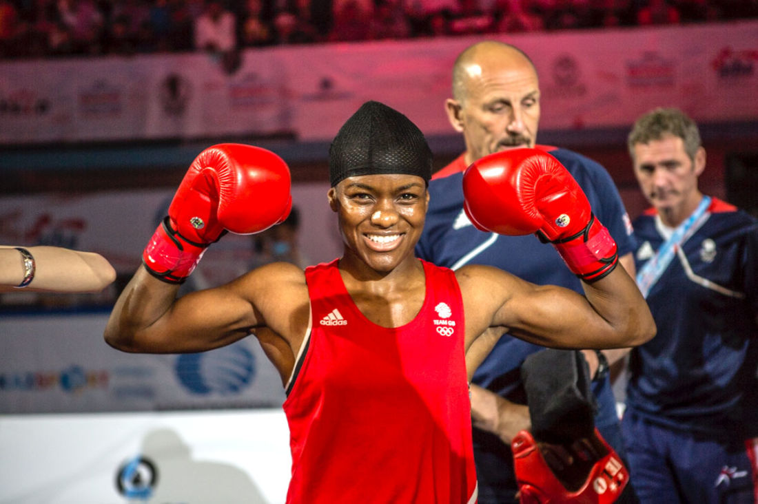  Photographie en couleur de Nicola Adams, vêtue d'un maillot rouge et de gants de boxe rouges, elle fait travailler ses biceps.