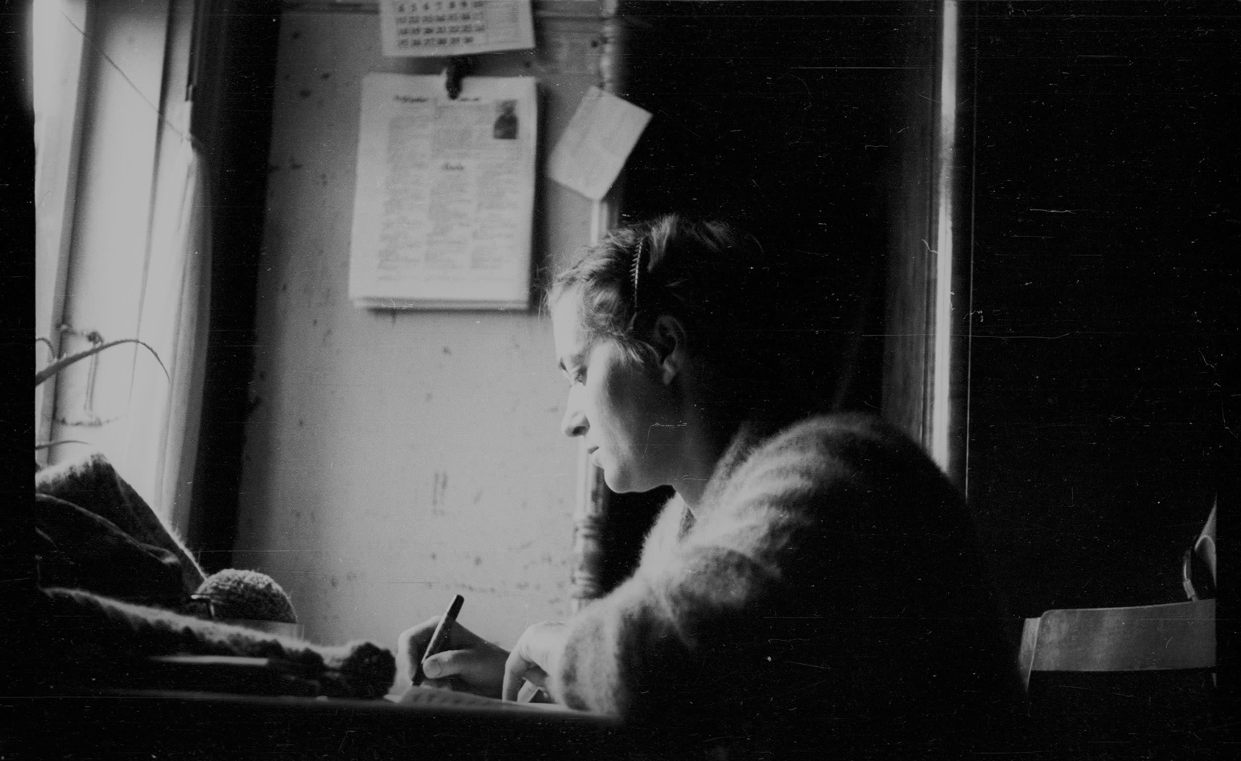 black and white photograph, a woman writing at a desk by a window.
