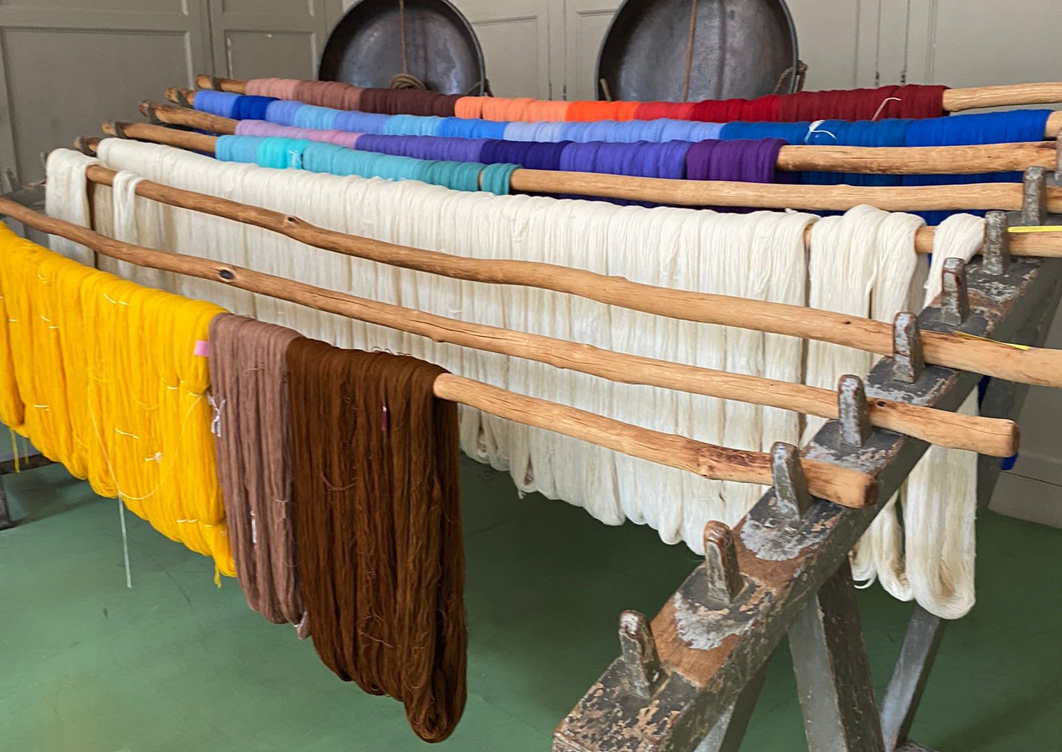 A wooden rack with bundles of wool dyed in different colours hanging and drying.