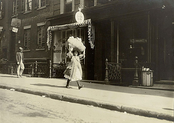 girl carrying bundle of clothing on her head in a city street