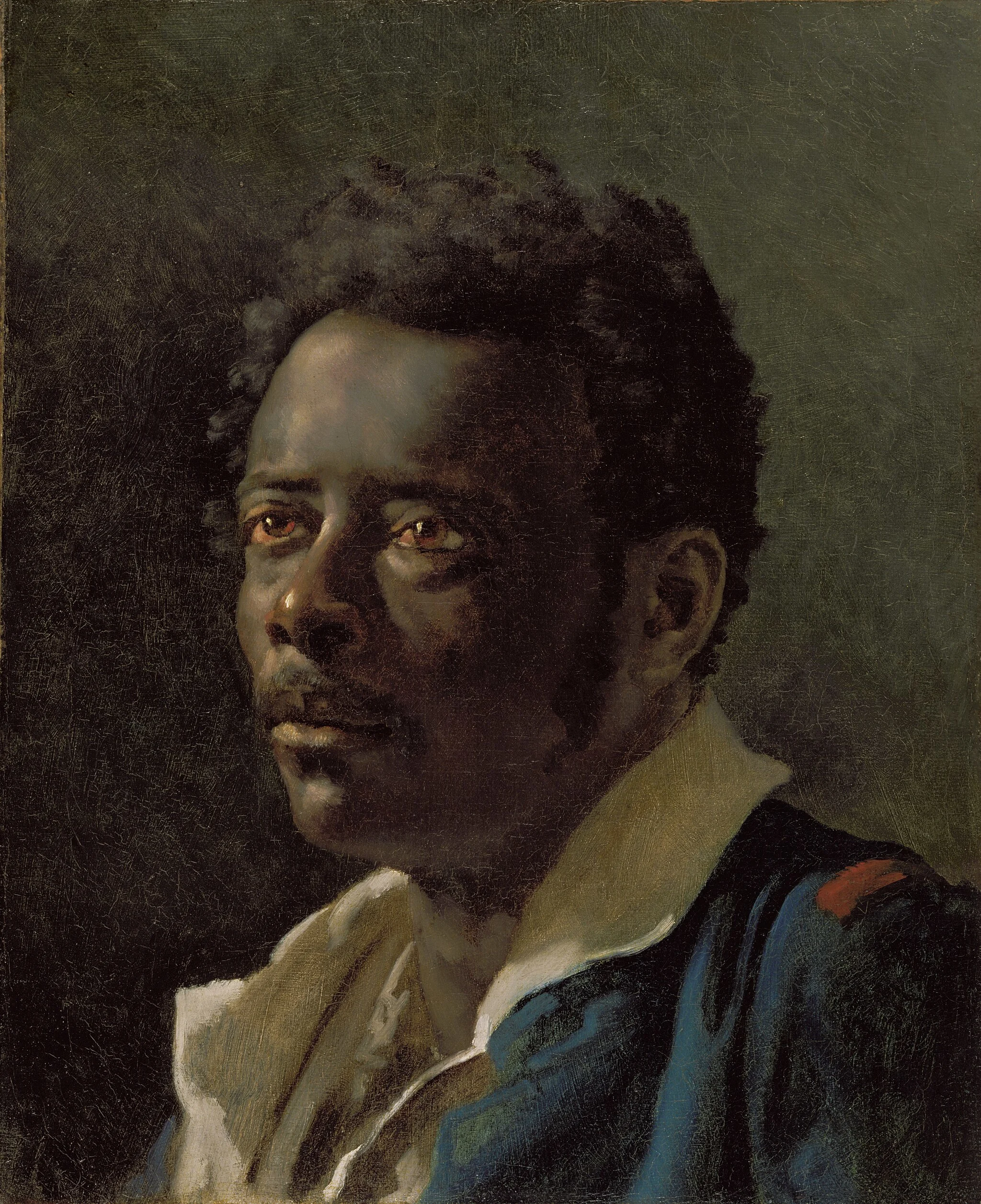 Joseph, avec une expression sérieuse, regarde vers le haut, vêtu d'un manteau foncé et d'une chemise blanche, sur un fond sombre.