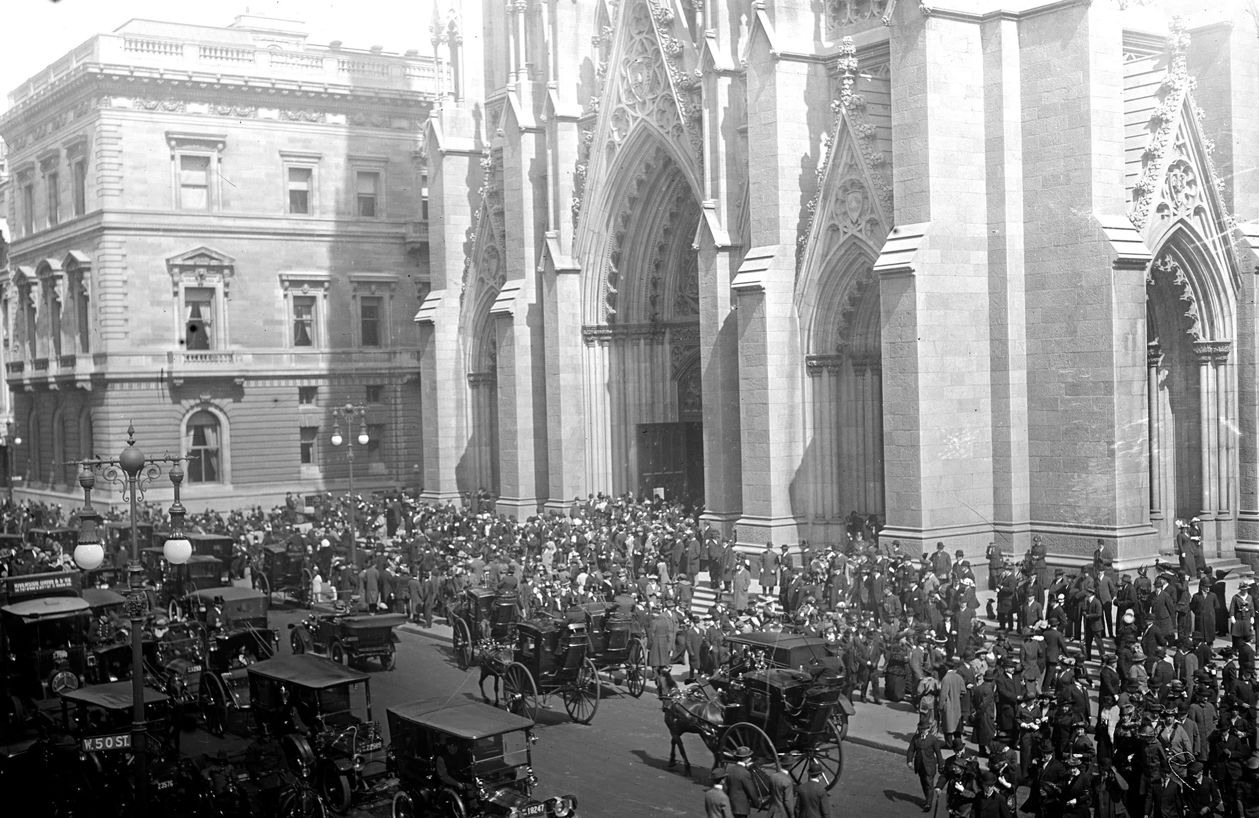 black and white photograph, a large number of horses and carriages outside a cathedral.