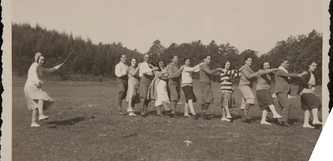 Young men and women dance together while a girl conducts the group holding a stick