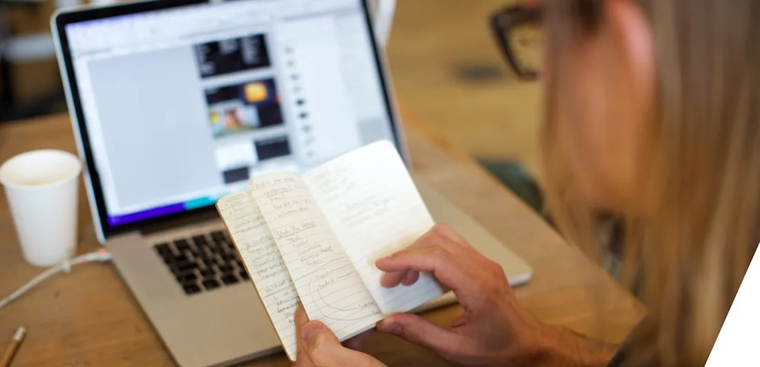 A person, seen from behind, looks at notes in a notebook