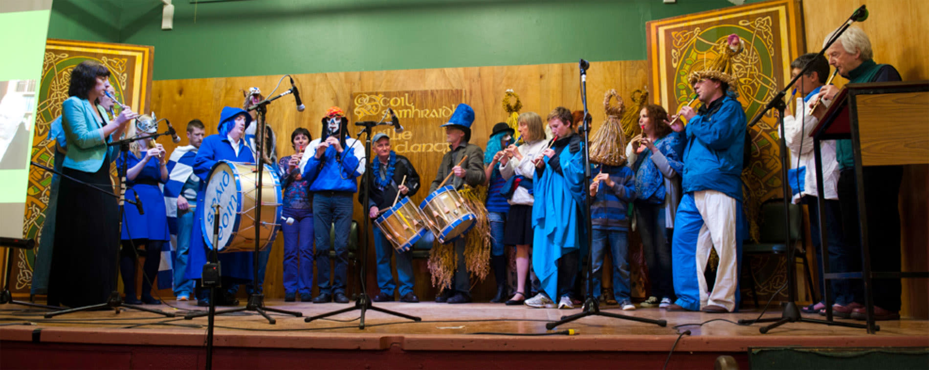 colour photograph, a large group of people wearing blue outfits on stage playing musical instruments.