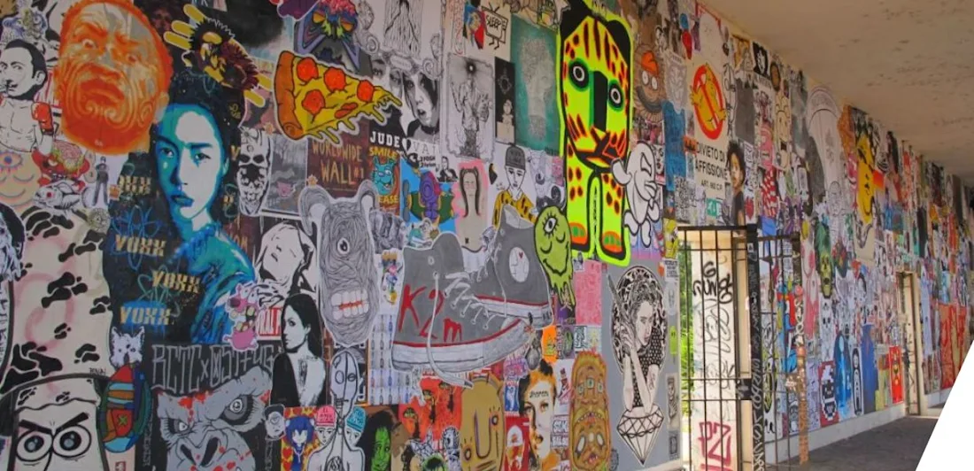 A long wall covered in colorful graffiti and street art, featuring various faces, patterns, and designs.