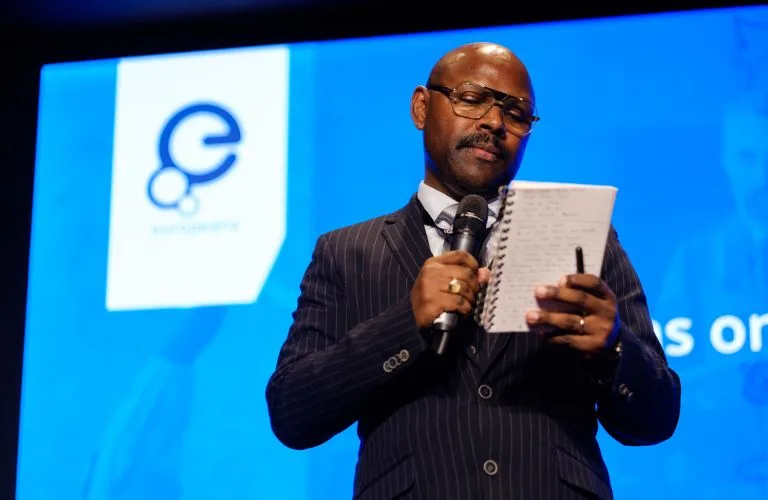 Mr Gee holding a microphone looking at a notebook, with the Europeana logo in the background.