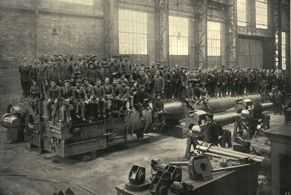 large crowd of men standing and sitting on large cannon in a factory building