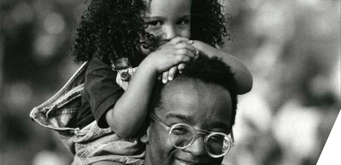 A smiling child sat on top of an adult's shoulders