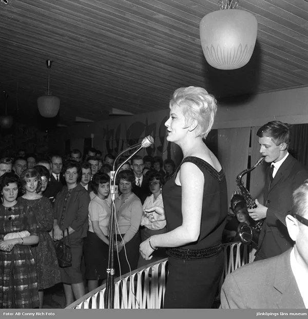 black and white photograph, a woman singing on stage while the audience watch.