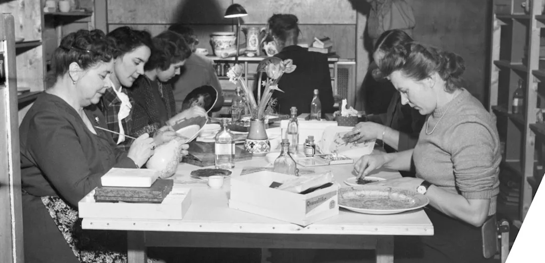 A group of women sat around a table painting porcelain 