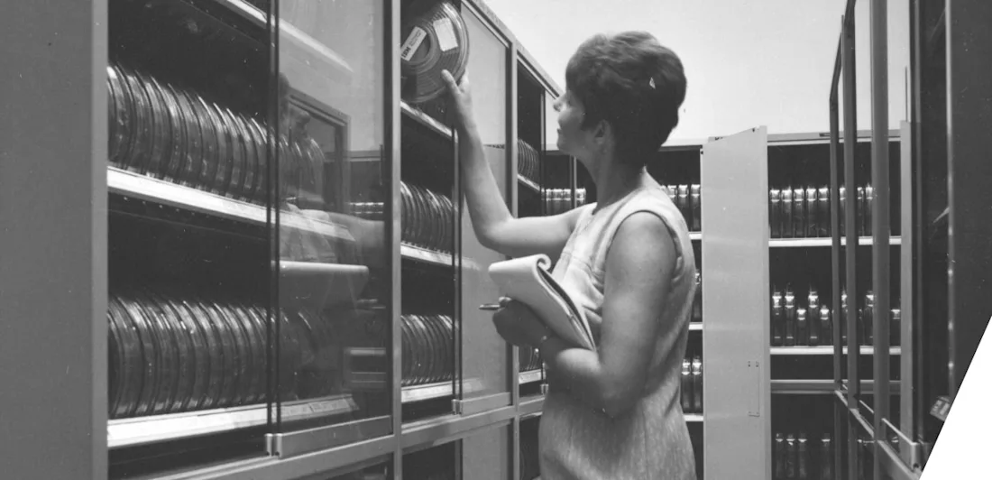 Someone taking a roll of film off some shelves while holding a clipboard