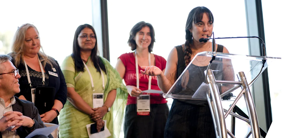 A person speaking at a podium while three people in the background look on