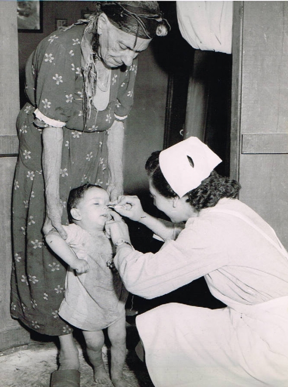 black and white photograph of a nurse treating a child's eye who is being held by an older woman
