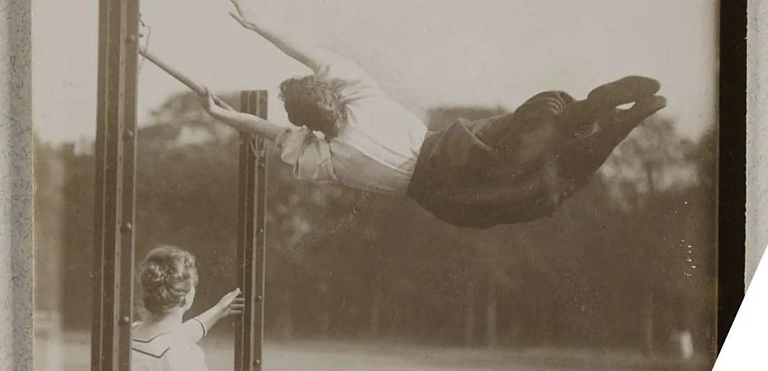 A gymnast swinging on a horizontal bar while another person looks on