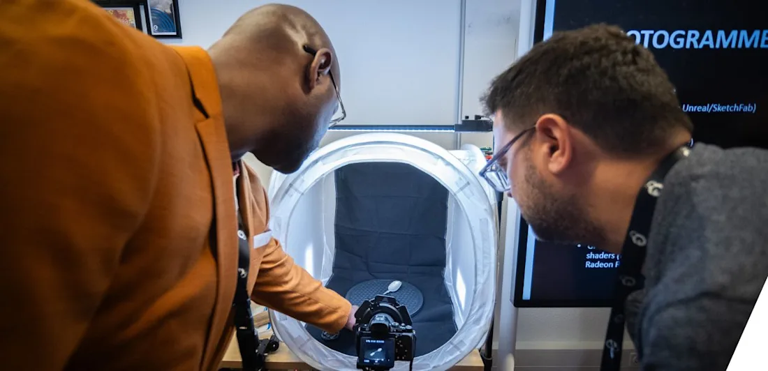 Two people looking towards a spoon being digitised in 3D