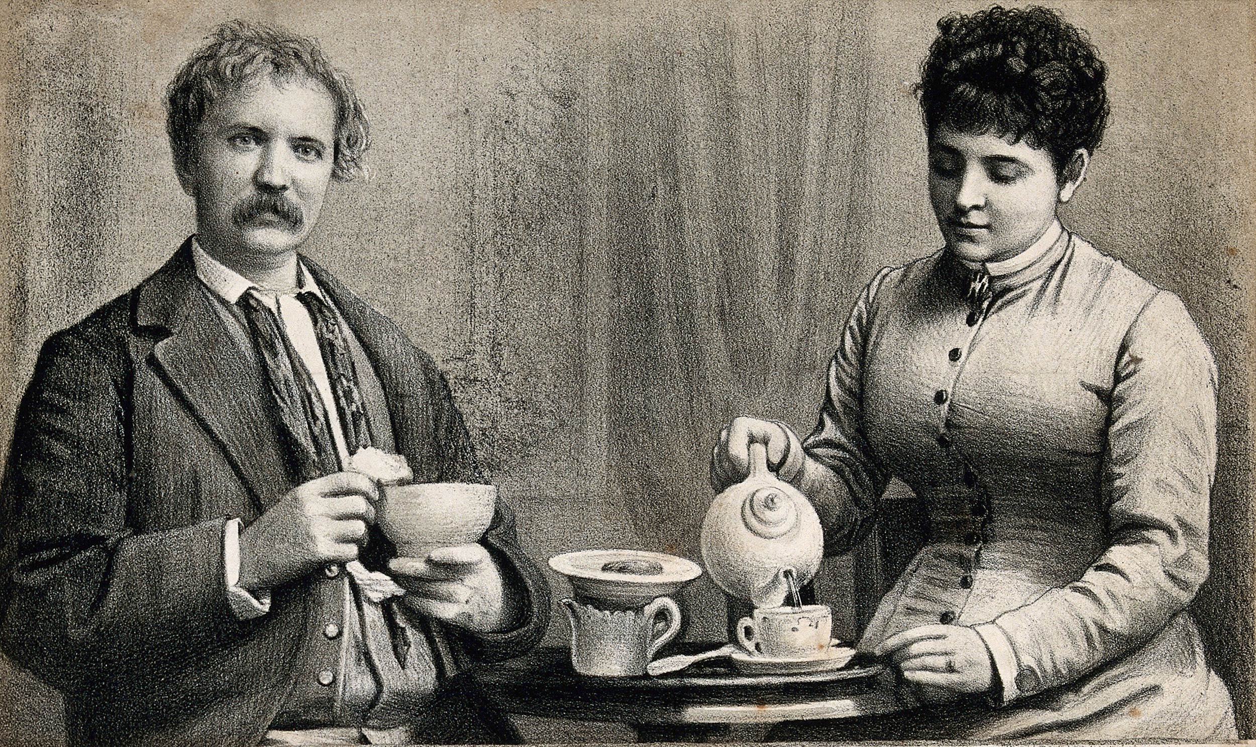 A couple sit at a table, the man is holding a bowl in his hand as the woman pours tea into a cup.