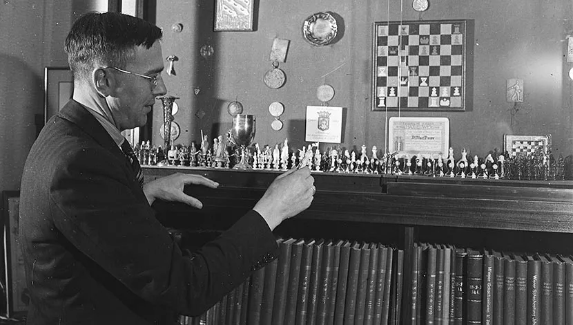 black and white photograph of Max Euwe who arranges chess pieces on a shelf