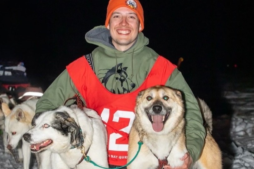 Wyatt Daley poses with several of his sled dogs while wearing a racing vest