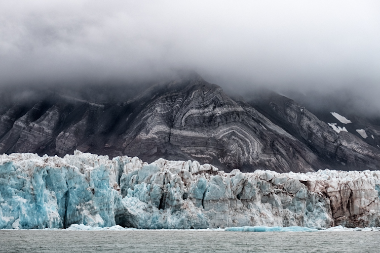 A large glacier sits at the bottom of a towering mountain in Svalbard, Norway