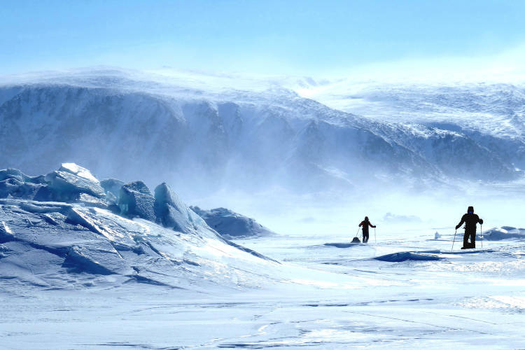 Two men ski across the windy sea ice landscape