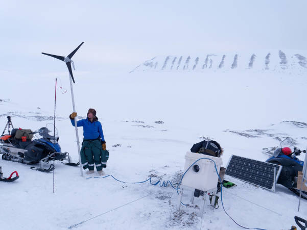 Two researchers looking out towards the tundra while another researcher is setting up equipment