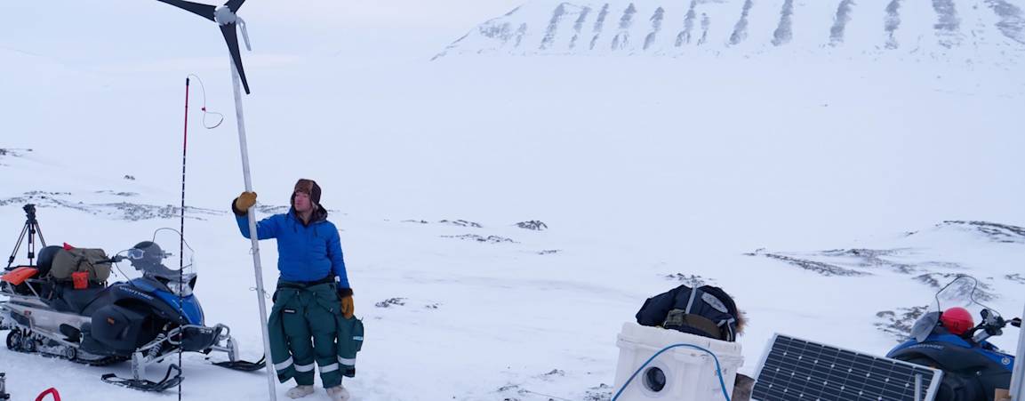 Two researchers looking out towards the tundra while another researcher is setting up equipment