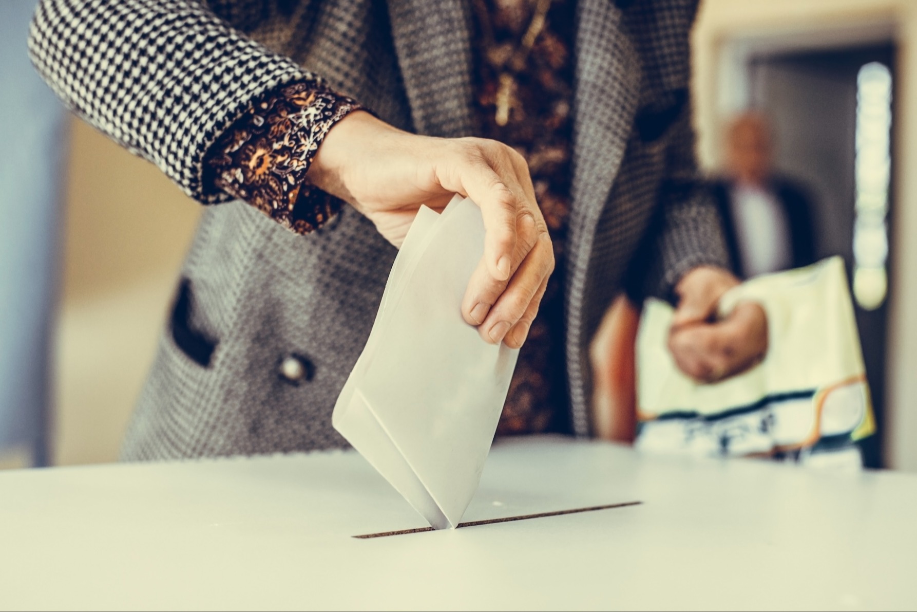 A woman's hand drops a paper ballot into a voting box