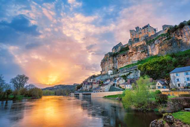 A view of Beynac-et-Cazenac village with medieval Chateau Beynac by a river on dramatic sunset, Dordogne, France