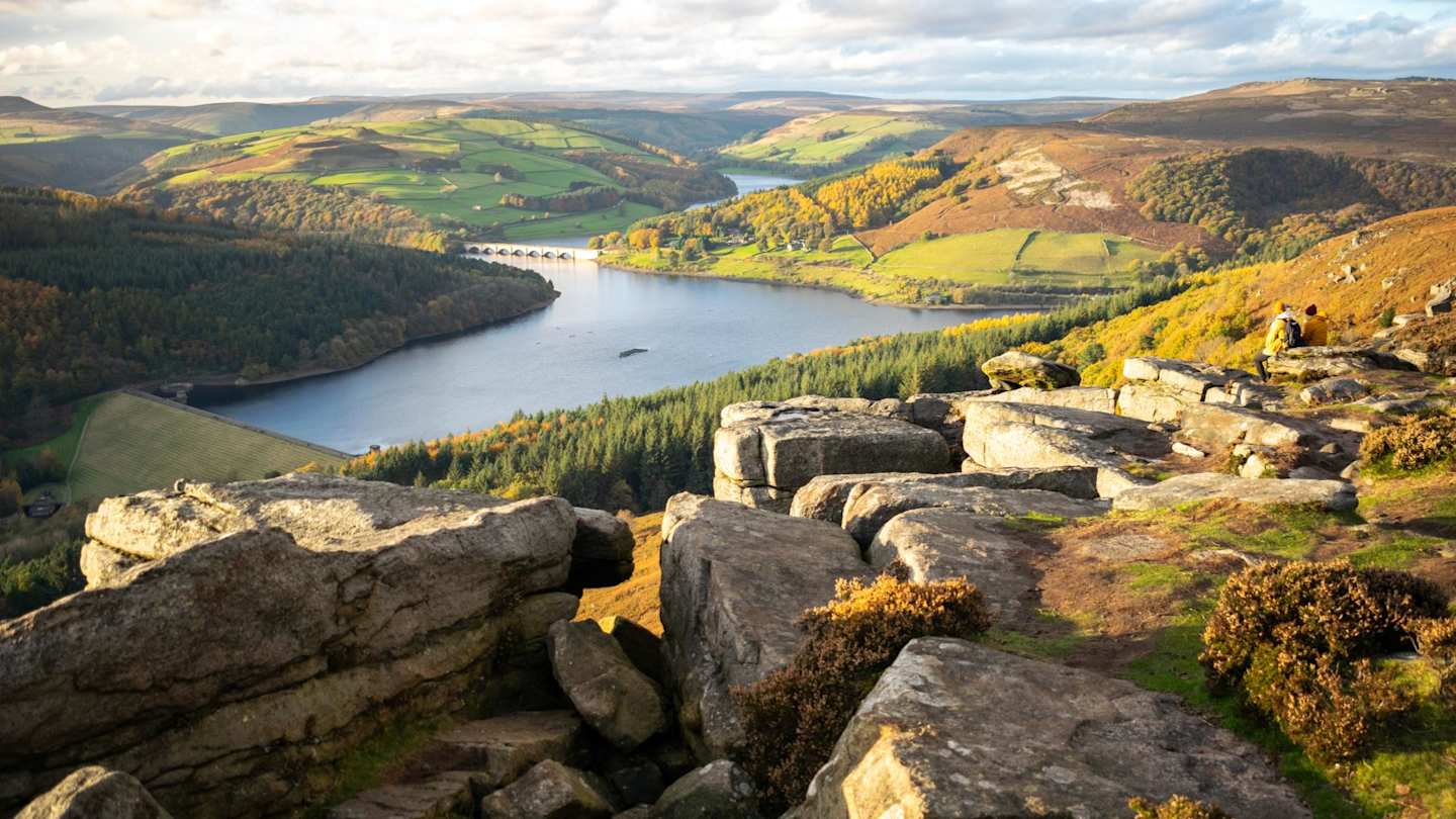 A view of a lake surrounded by tall hills and rocks from up high in the Peak District, England, UK