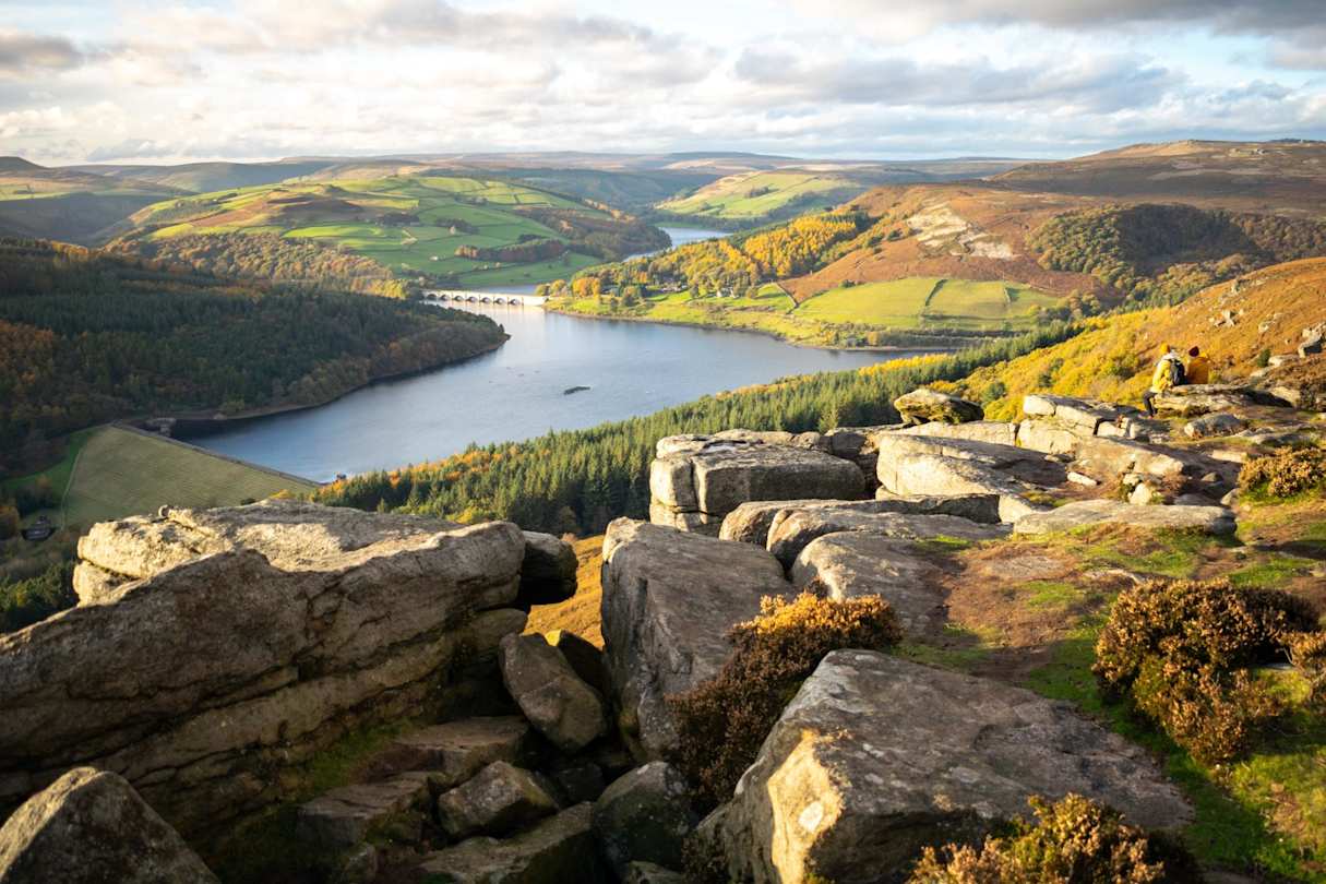A view of a lake surrounded by tall hills and rocks from up high in the Peak District, England, UK