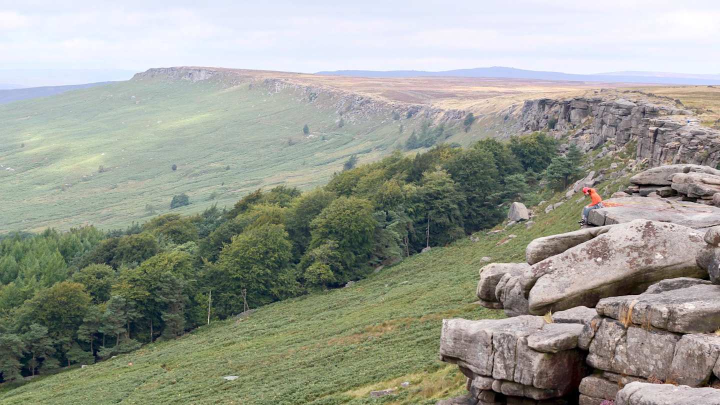A person sitting on a stone wall by large green fields in Derbyshire, England, UK