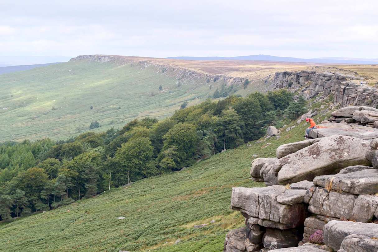 A person sitting on a stone wall by large green fields in Derbyshire, England, UK