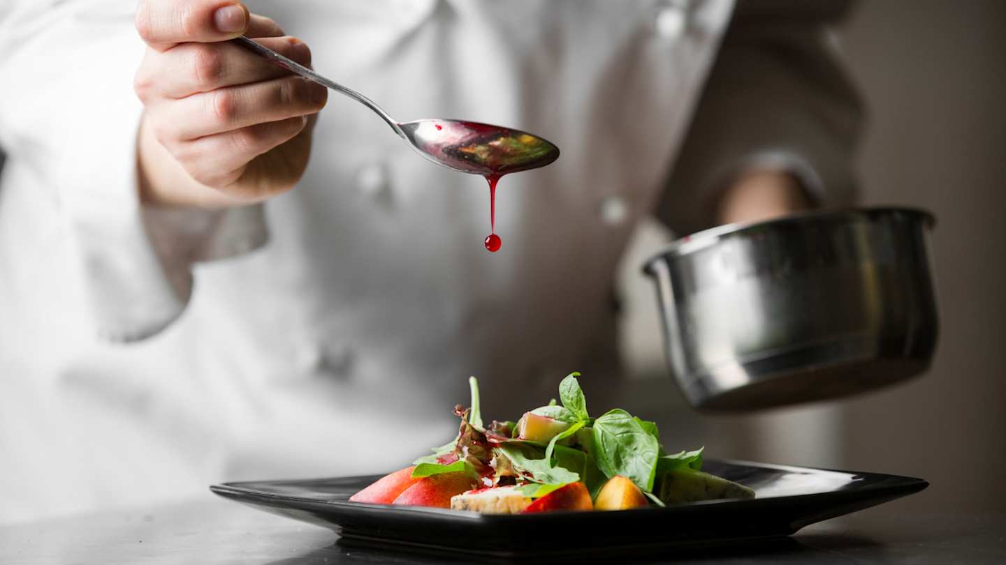 A close up view of a chef drizzling red sauce over a neat dish at a London restaurant