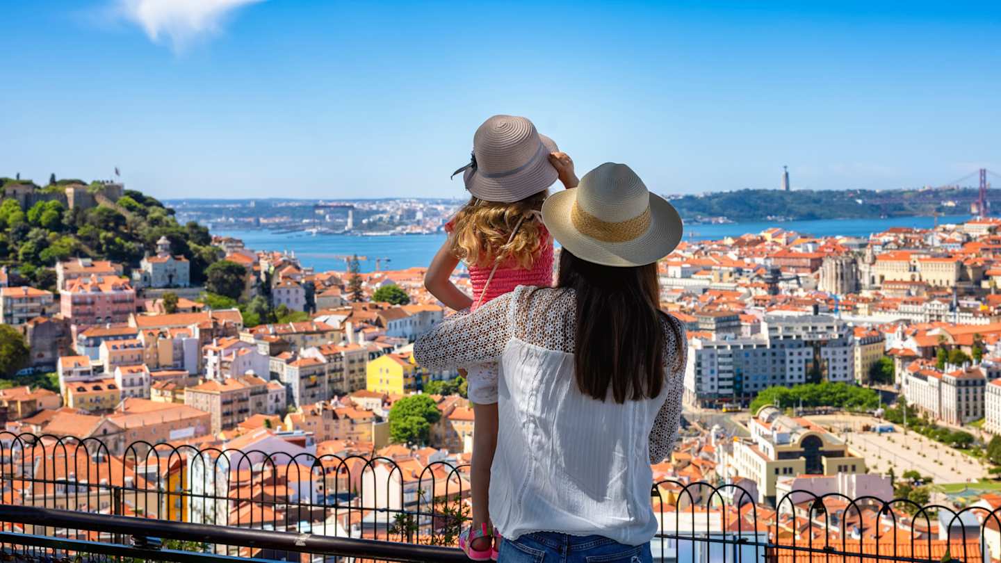 A tourist mother and her daughter enjoy the view of the cityscape, with colourful houses and roofs, Lisbon, Portugal