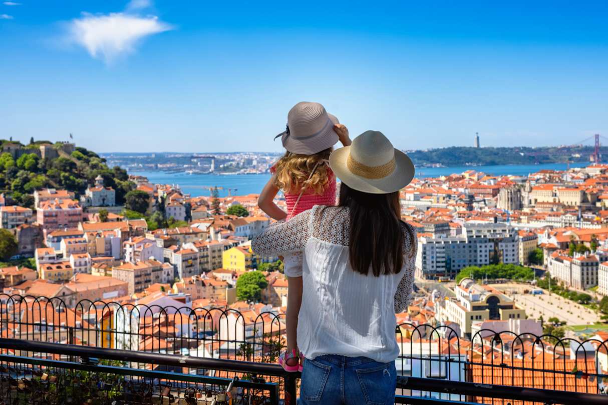 A tourist mother and her daughter enjoy the view of the cityscape, with colourful houses and roofs, Lisbon, Portugal