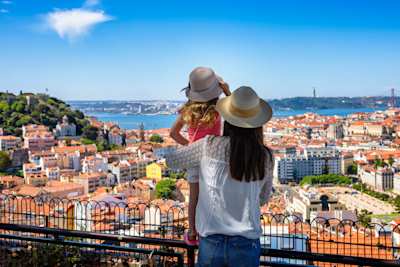 A tourist mother and her daughter enjoy the view of the cityscape, with colourful houses and roofs, Lisbon, Portugal