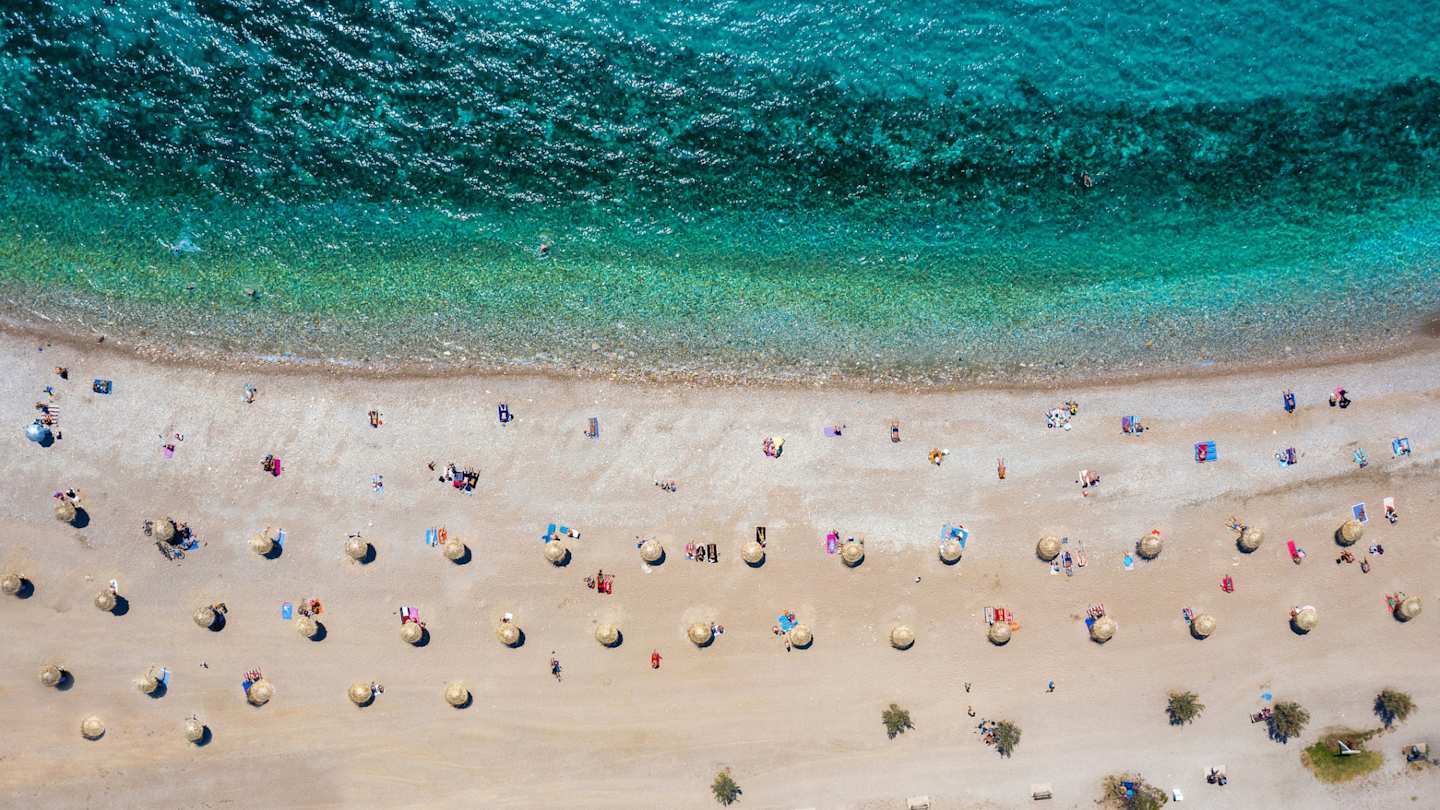 A bird's eye view of the turquoise sea and white sand with parasols at Glyfada Beach, Athens, Greece