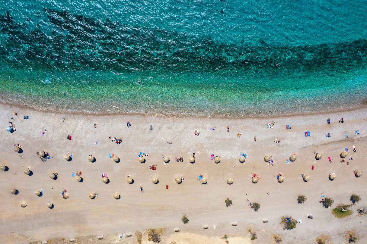 A bird's eye view of the turquoise sea and white sand with parasols at Glyfada Beach, Athens, Greece