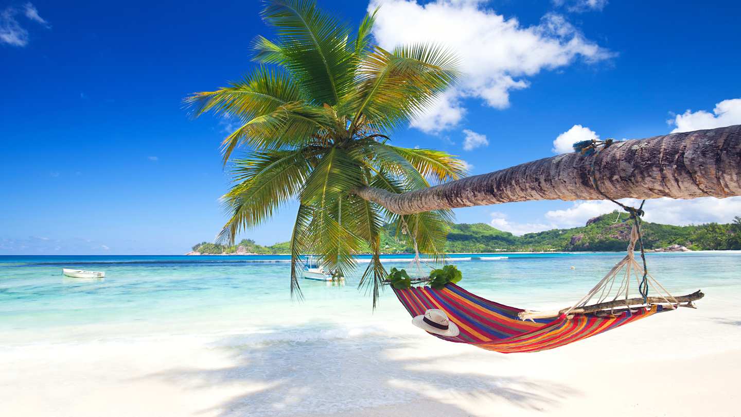 A hat sitting on a hammock tied to a horizontal palm tree on a pristine beach in the Seychelles in August
